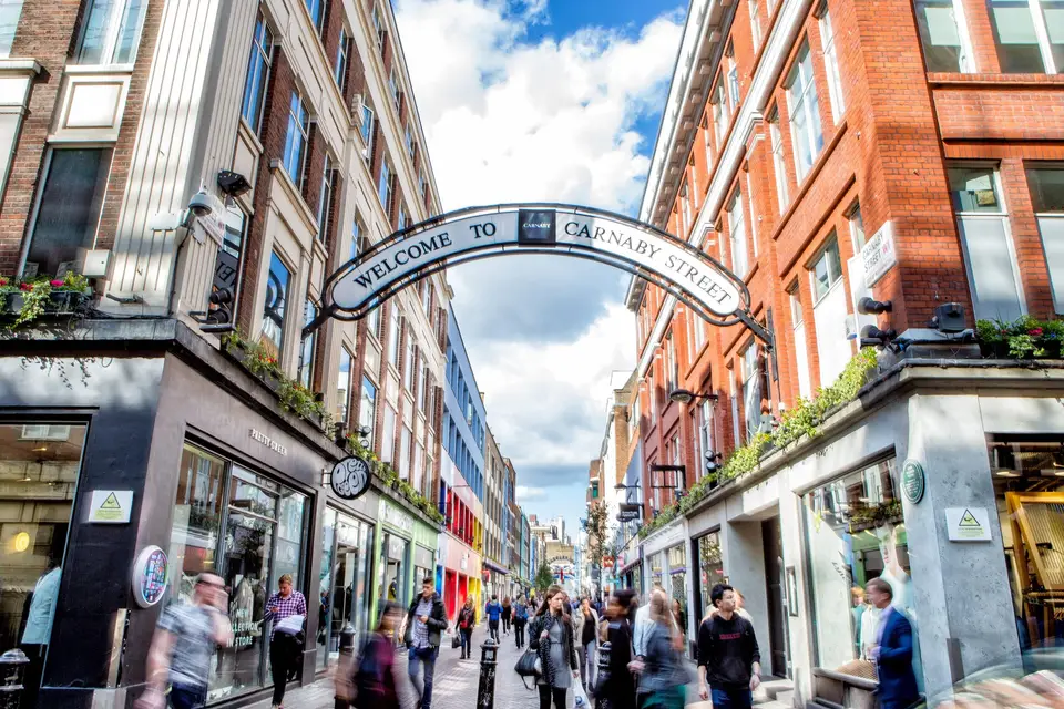 Shoppers walking under the Welcome to Carnaby Street arch on a sunny day