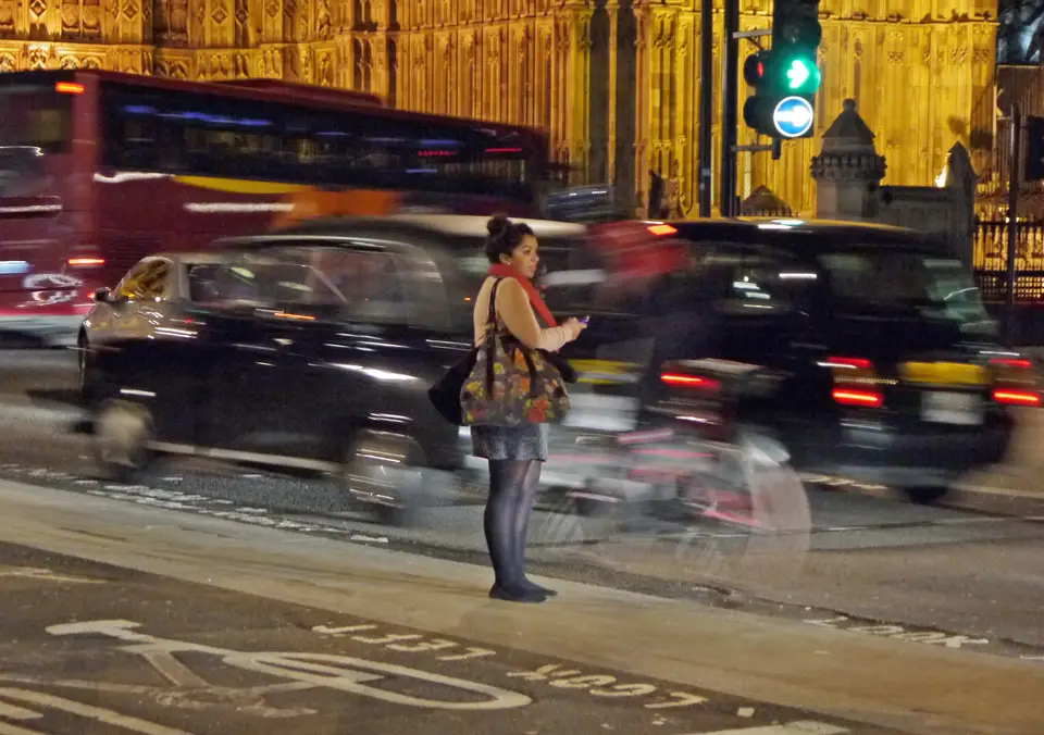 A pedestrian on her phone on a London street at night