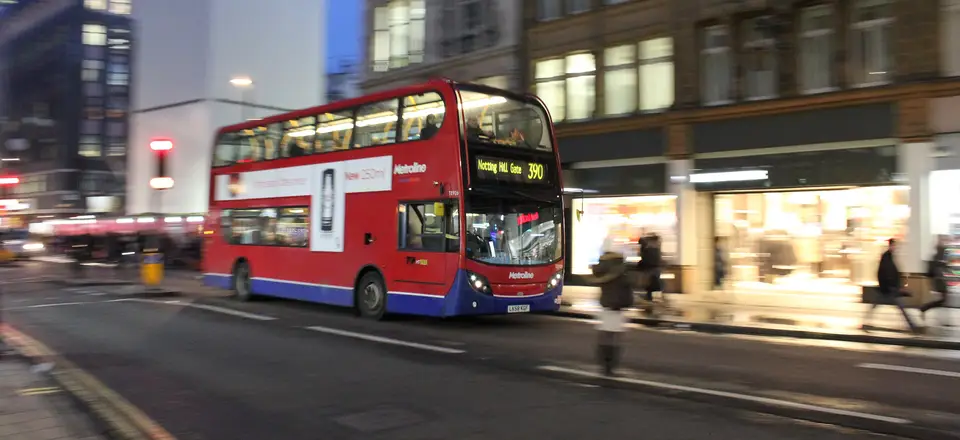 A red bus passing shops on a busy London street in the morning